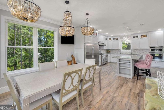 dining area with crown molding, sink, light hardwood / wood-style floors, and an inviting chandelier