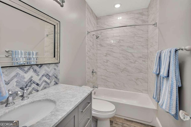 full bathroom featuring tasteful backsplash, vanity, tiled shower / bath combo, hardwood / wood-style floors, and toilet