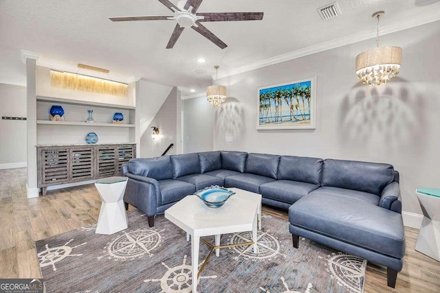 living room featuring ornamental molding, built in shelves, ceiling fan with notable chandelier, a textured ceiling, and wood-type flooring