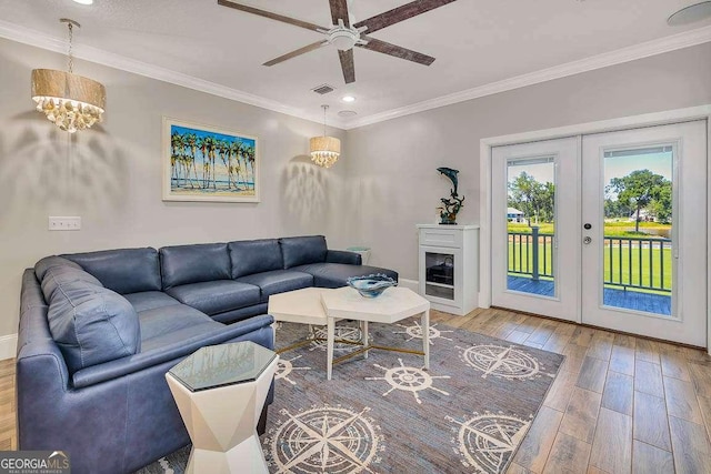 living room featuring french doors, wood-type flooring, ceiling fan with notable chandelier, and ornamental molding