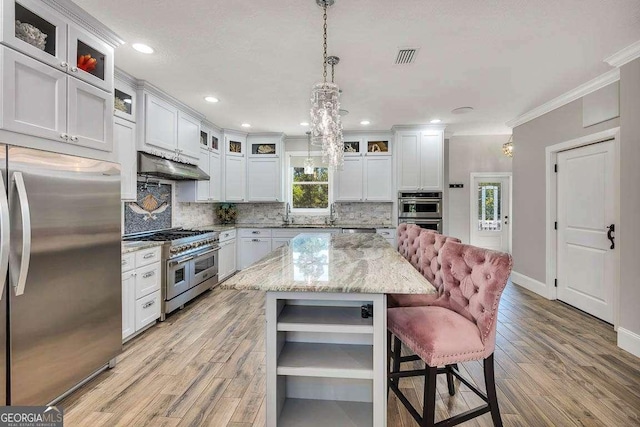 kitchen with a center island, a healthy amount of sunlight, light stone counters, white cabinets, and appliances with stainless steel finishes