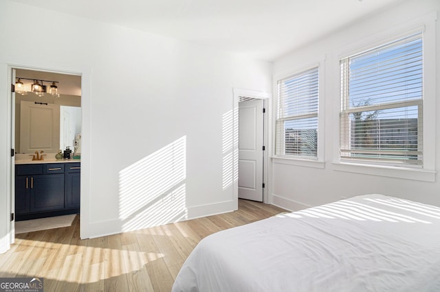 bedroom featuring ensuite bathroom, light hardwood / wood-style flooring, multiple windows, and sink