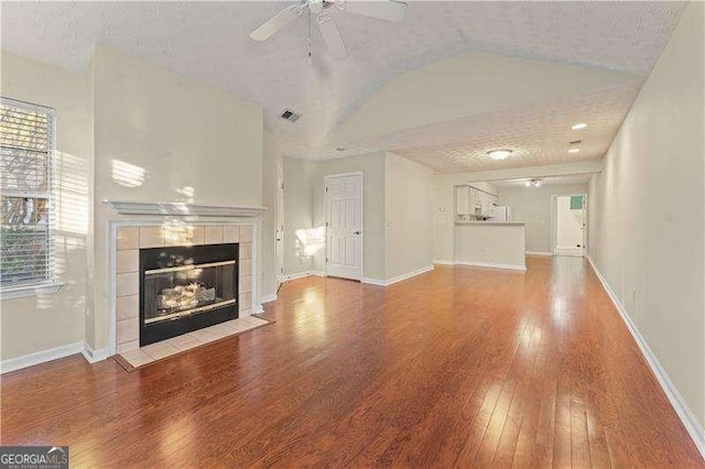 unfurnished living room featuring hardwood / wood-style floors, ceiling fan, a fireplace, and a textured ceiling