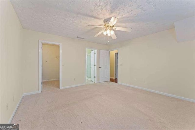 unfurnished bedroom with ceiling fan, a spacious closet, a textured ceiling, light colored carpet, and a closet