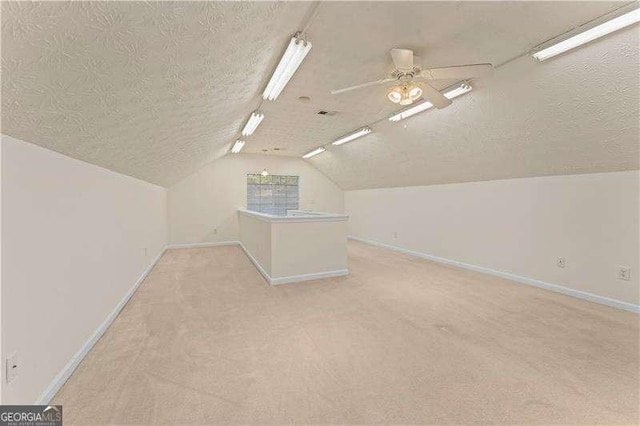 additional living space with vaulted ceiling, light carpet, ceiling fan, and a textured ceiling