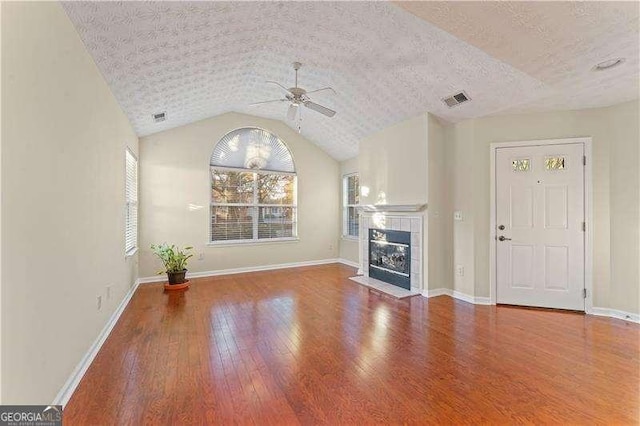 unfurnished living room featuring hardwood / wood-style floors, lofted ceiling, ceiling fan, a fireplace, and a textured ceiling