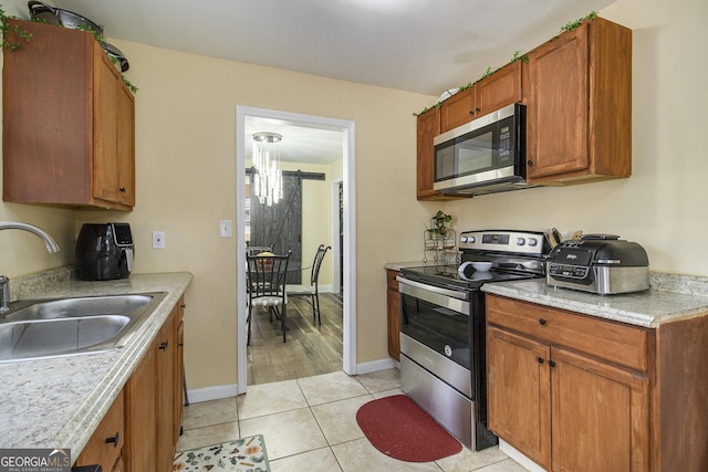 kitchen with sink, light tile patterned floors, stainless steel appliances, and a notable chandelier