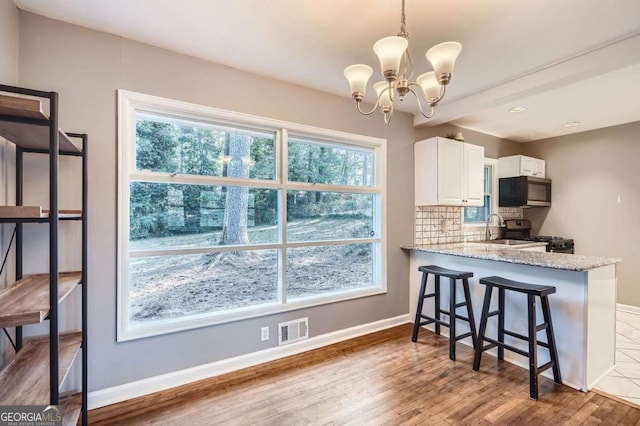 kitchen featuring pendant lighting, white cabinets, light wood-type flooring, kitchen peninsula, and stainless steel appliances