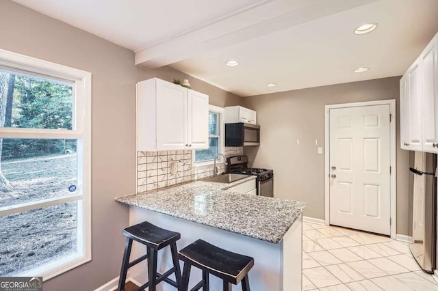 kitchen with backsplash, light stone countertops, appliances with stainless steel finishes, white cabinetry, and kitchen peninsula