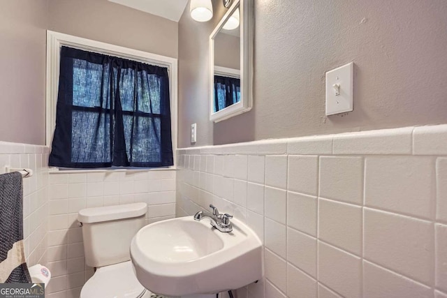 bathroom featuring toilet, tile walls, and sink