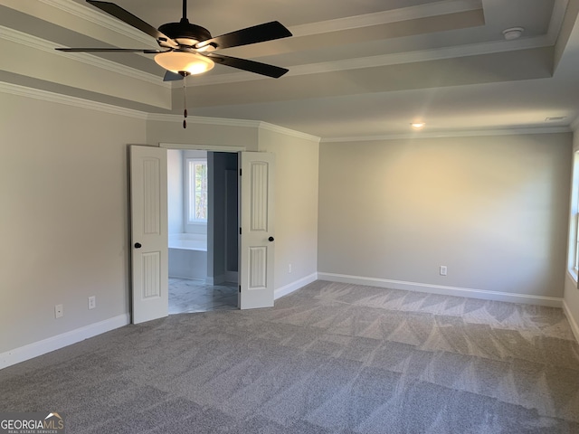 carpeted empty room with ceiling fan, ornamental molding, and a raised ceiling