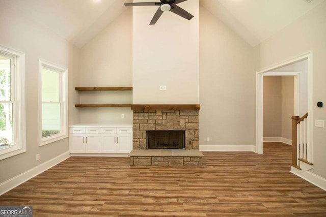 unfurnished living room with hardwood / wood-style flooring, ceiling fan, a stone fireplace, and high vaulted ceiling