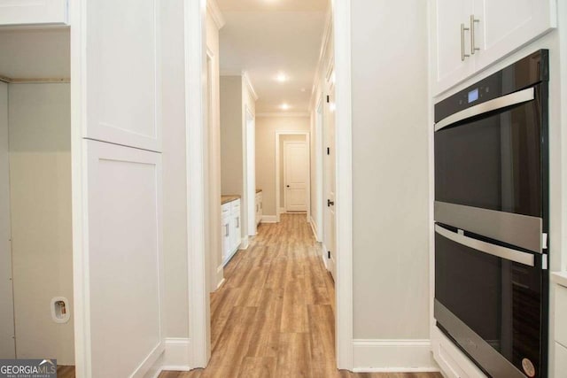 interior space featuring white cabinets, light wood-type flooring, ornamental molding, and double oven