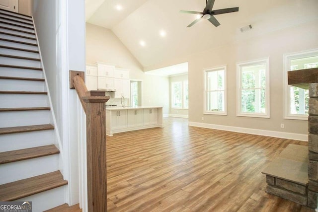 unfurnished living room with ceiling fan, light hardwood / wood-style flooring, high vaulted ceiling, and sink