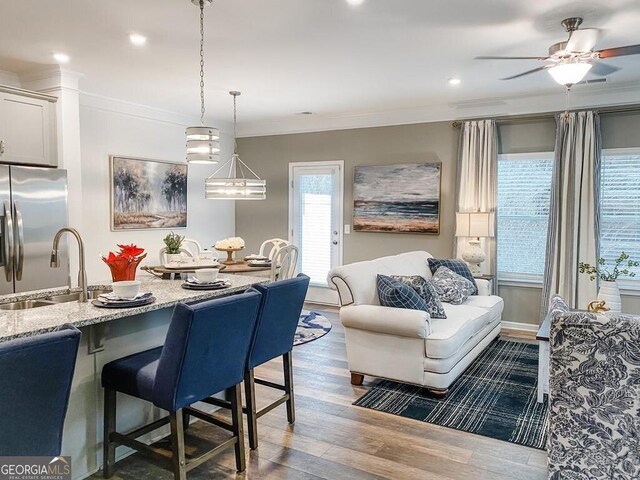 dining space with crown molding, sink, ceiling fan, and wood-type flooring