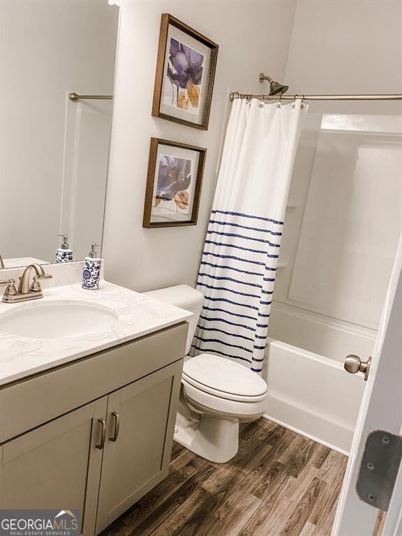 full bathroom featuring hardwood / wood-style floors, vanity, shower / tub combo, and toilet