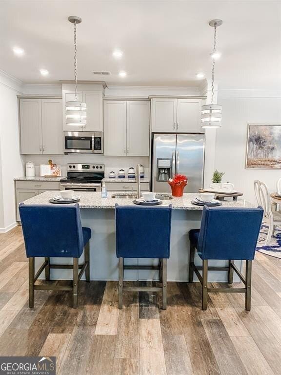 kitchen with a kitchen island with sink, wood-type flooring, and appliances with stainless steel finishes