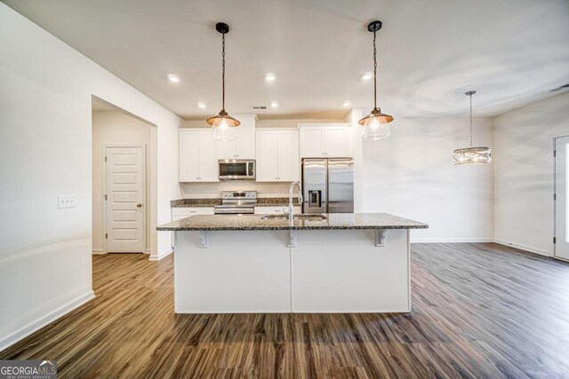 kitchen with sink, dark hardwood / wood-style flooring, dark stone counters, a center island with sink, and appliances with stainless steel finishes