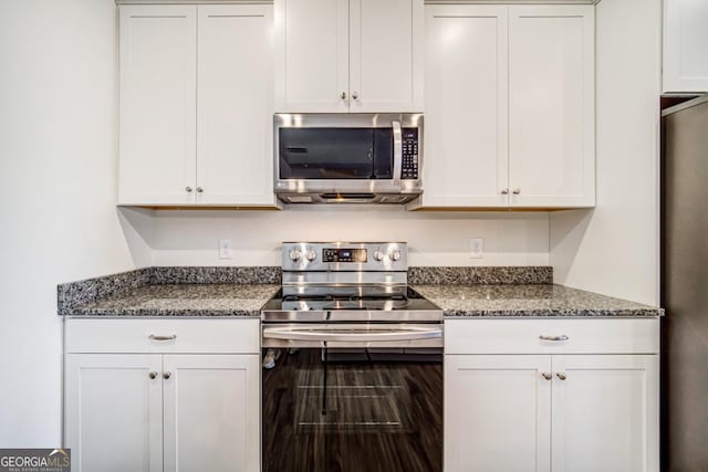 kitchen featuring white cabinets, stainless steel appliances, and dark stone counters