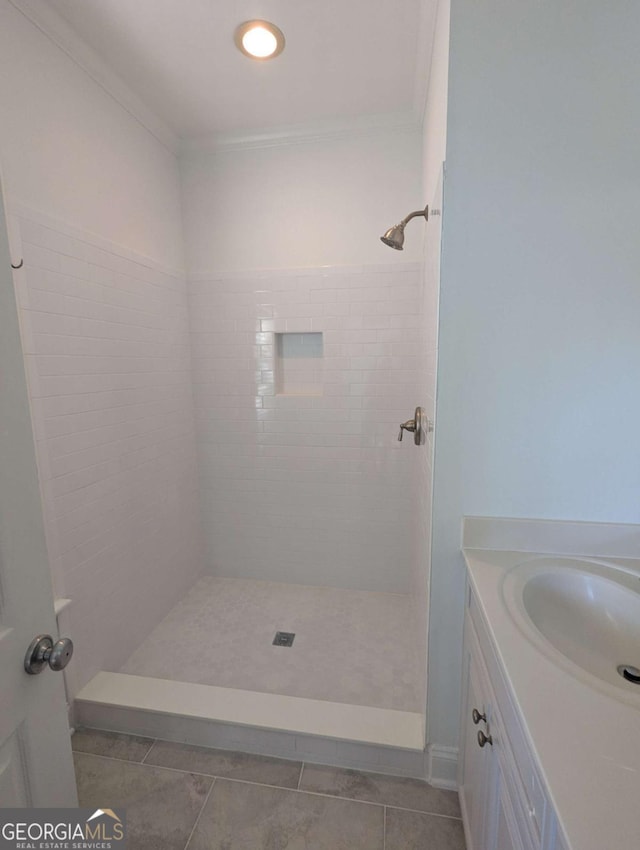 bathroom featuring tile patterned flooring, vanity, crown molding, and tiled shower