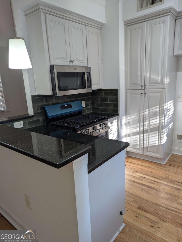 kitchen with white cabinets, appliances with stainless steel finishes, tasteful backsplash, and light hardwood / wood-style flooring