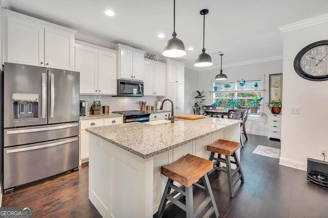 kitchen featuring light stone countertops, stainless steel appliances, decorative light fixtures, a center island with sink, and white cabinets