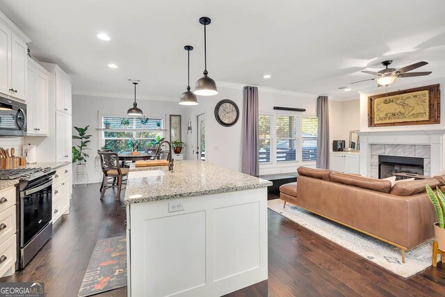 kitchen featuring white cabinetry, stainless steel range, light stone counters, an island with sink, and decorative light fixtures