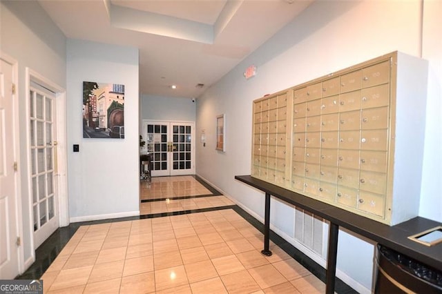 hall with a tray ceiling, french doors, light tile patterned floors, and a mail area