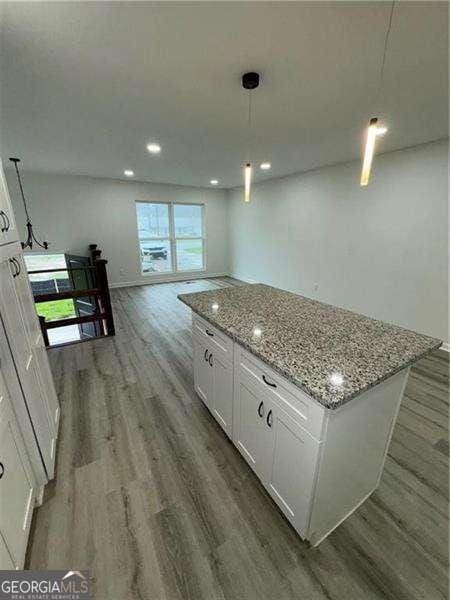 kitchen with light stone countertops, decorative light fixtures, white cabinets, a center island, and dark hardwood / wood-style floors