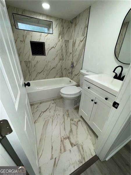 full bathroom featuring vanity, tiled shower / bath combo, and toilet