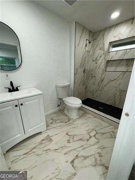 bathroom with vanity, toilet, and a tile shower