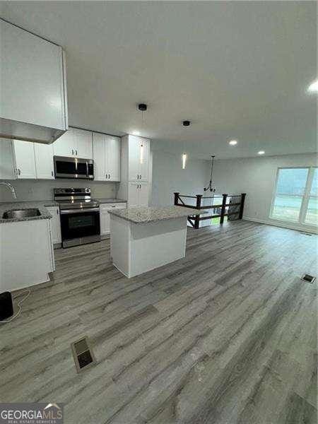 kitchen with decorative light fixtures, white cabinetry, appliances with stainless steel finishes, and light hardwood / wood-style flooring