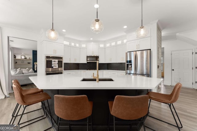 kitchen with sink, stainless steel appliances, backsplash, a large island with sink, and light hardwood / wood-style floors