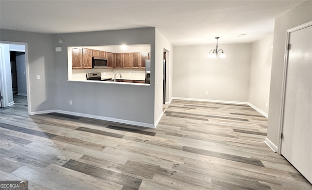 kitchen featuring stainless steel appliances, sink, decorative light fixtures, an inviting chandelier, and light hardwood / wood-style flooring