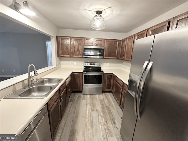 kitchen featuring kitchen peninsula, appliances with stainless steel finishes, sink, pendant lighting, and light hardwood / wood-style flooring