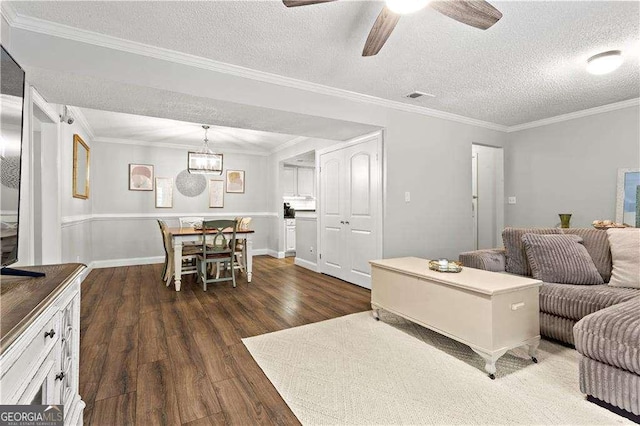 living room with crown molding, ceiling fan, dark wood-type flooring, and a textured ceiling