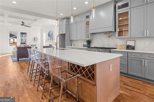 kitchen with a kitchen island with sink, pendant lighting, wood-type flooring, and custom range hood