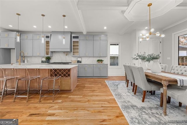 kitchen featuring hanging light fixtures, gray cabinets, wall chimney range hood, and a breakfast bar