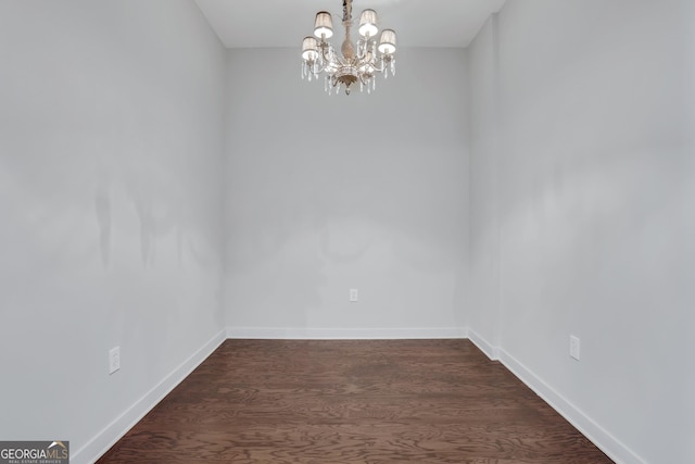 unfurnished room featuring dark wood-type flooring and an inviting chandelier