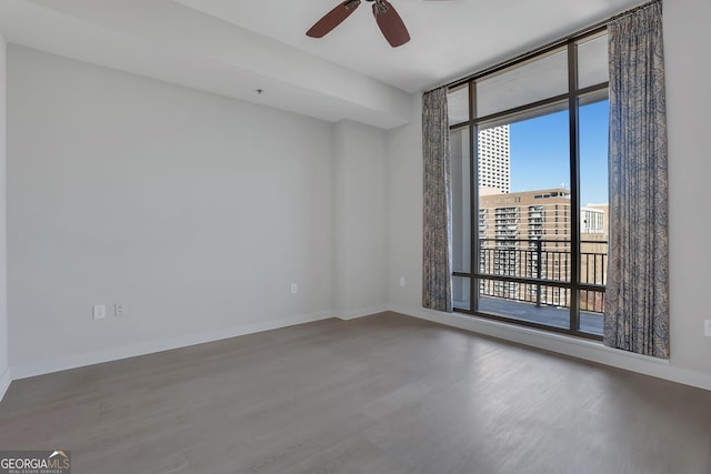 empty room with hardwood / wood-style floors, a wall of windows, and ceiling fan