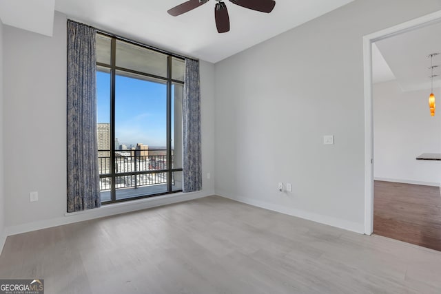 unfurnished room with a wall of windows, ceiling fan, and light wood-type flooring