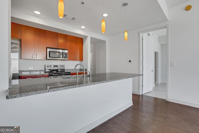 kitchen featuring dark wood-type flooring, sink, dark stone countertops, appliances with stainless steel finishes, and kitchen peninsula