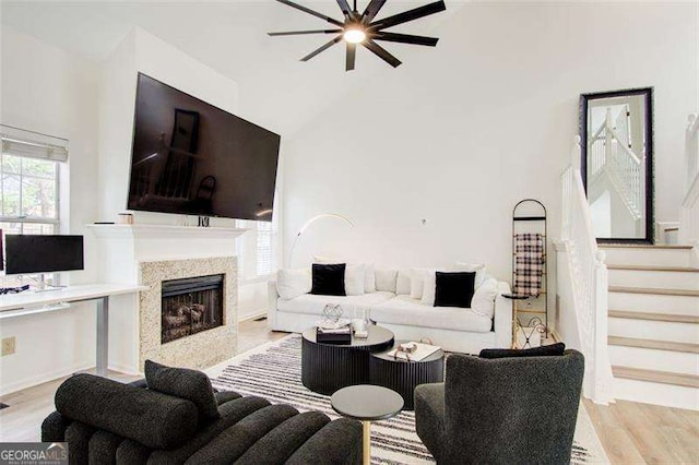 living room with a high end fireplace, light wood-type flooring, ceiling fan, and lofted ceiling