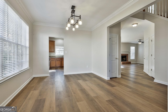 unfurnished dining area with a fireplace, ceiling fan with notable chandelier, dark hardwood / wood-style floors, and ornamental molding