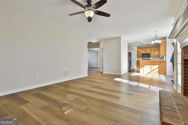 unfurnished living room featuring a fireplace, light hardwood / wood-style flooring, and ceiling fan with notable chandelier