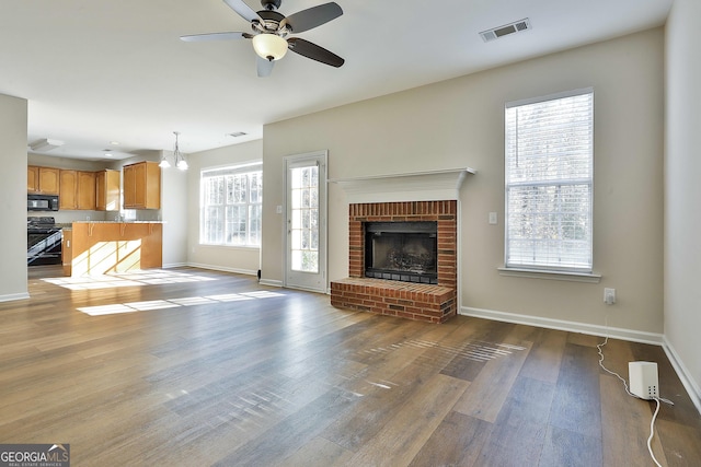 unfurnished living room featuring hardwood / wood-style flooring, ceiling fan with notable chandelier, a fireplace, and a wealth of natural light