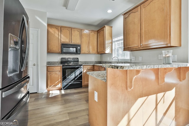 kitchen featuring black appliances, light wood-type flooring, light stone counters, kitchen peninsula, and a breakfast bar area