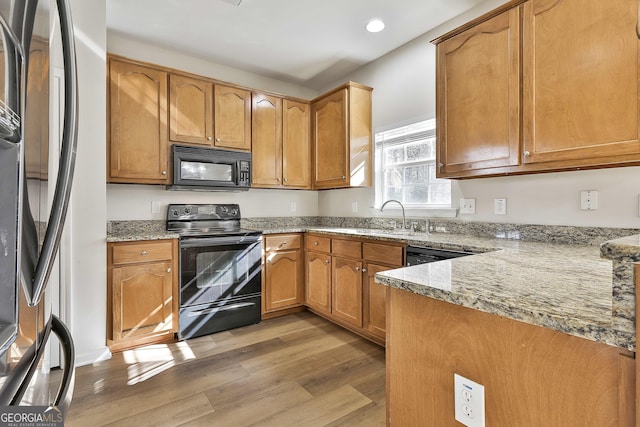 kitchen with light stone countertops, light hardwood / wood-style flooring, black appliances, and sink