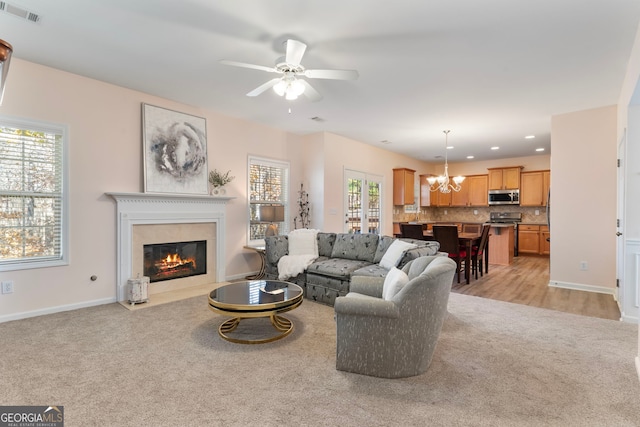 living room featuring light carpet, plenty of natural light, and ceiling fan with notable chandelier