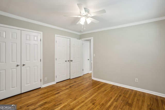 unfurnished bedroom featuring ceiling fan, crown molding, wood-type flooring, and two closets